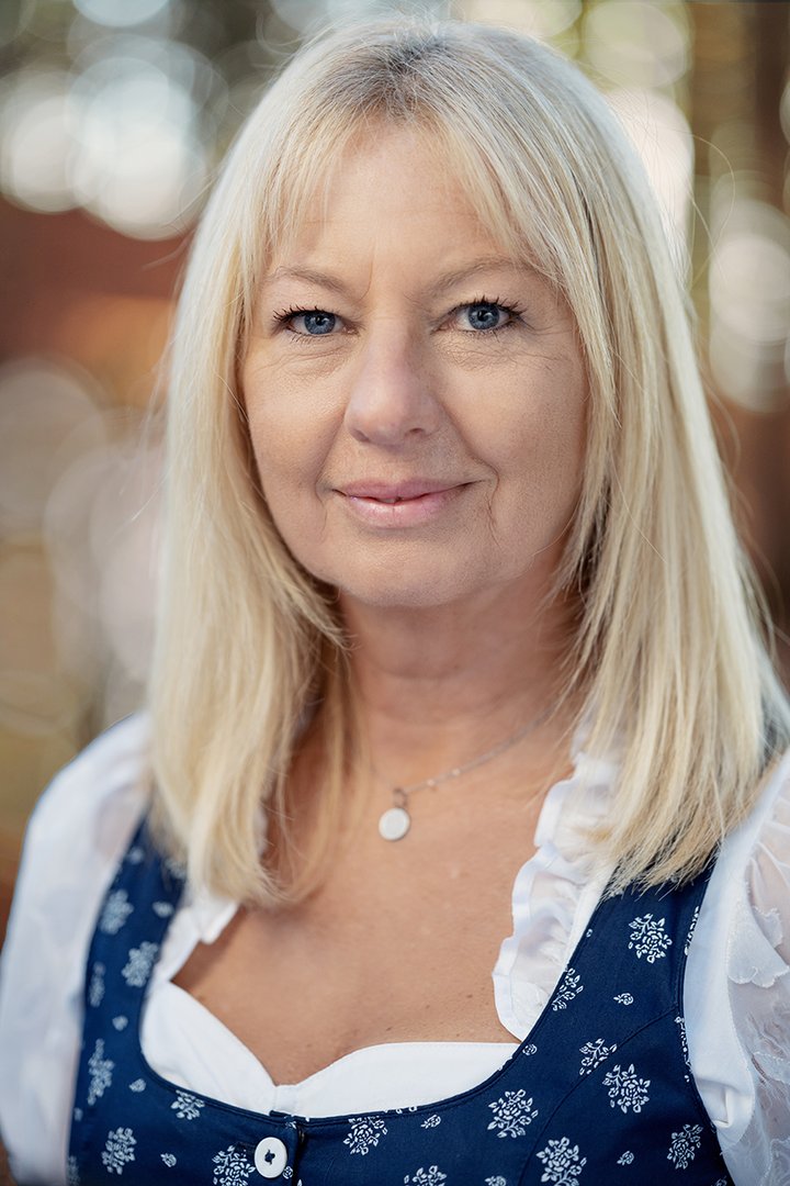 Portraitfoto von Hausruckwald-Teammitglied Karin Klement. Blonde, schulterlange Haare, dunkelblaues Dirndl mit weißer Rüschenbluse. Sie lächelt und schaut direkt in die Kamera.